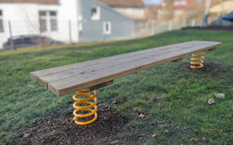Federndes Balancierbrett aus Holz auf der Wiese im Garten des Kindergartens